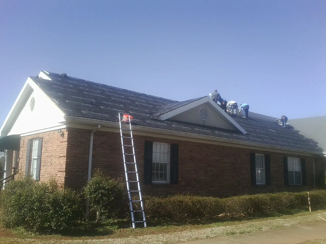 Crew tearing shingles off a brick ranch roof with a ladder set — Emergency Roof Repair work by our crew in Scandia