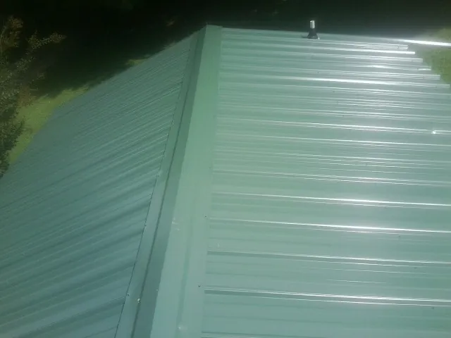 New green metal panels meeting at the ridge of a roof — Flat Roof Repair work by our crew in Scandia