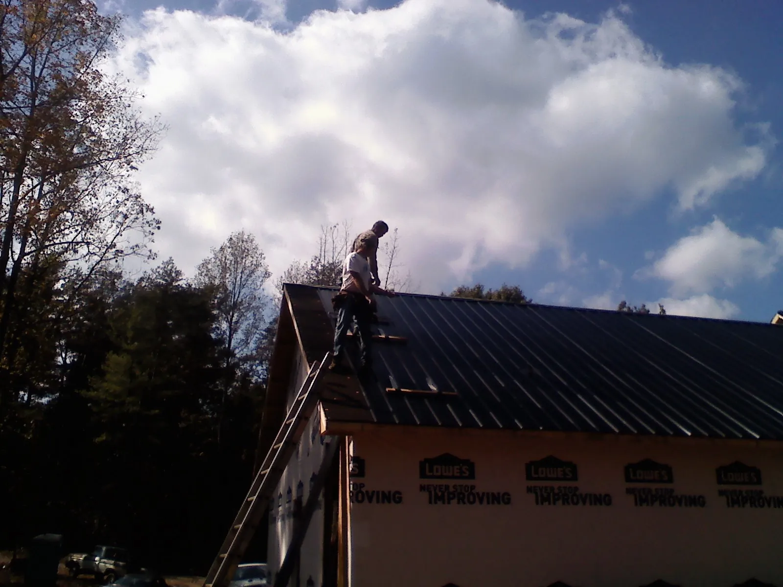 Roofer fastening dark metal panels high against a cloudy sky, from a Roof Inspection job in Scandia