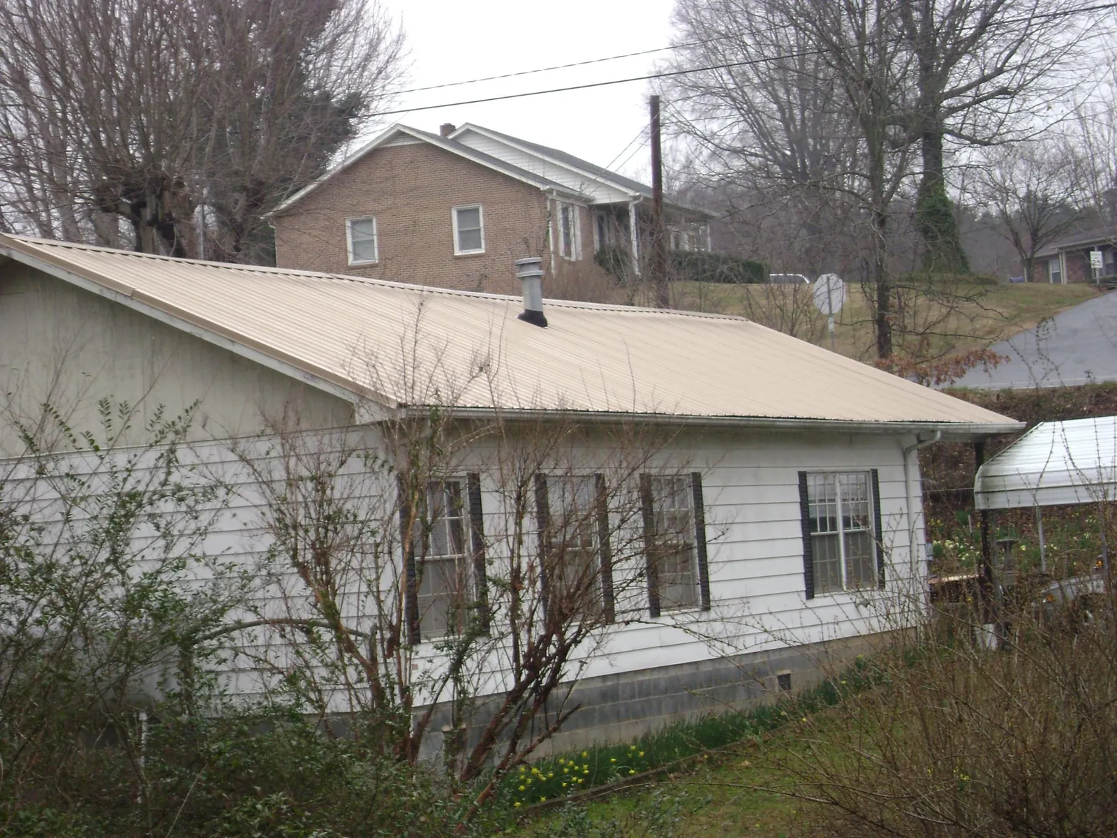 Tan metal roof on a white sided house set into a hillside — Commercial Roofing by Roofing Brothers in Scandia